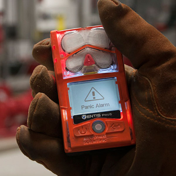 Gloved hand holding a VentisPro5 multi gas monitor displaying panic alarm notification